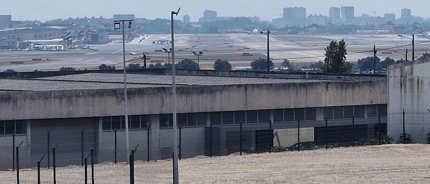 Aircraft on the apron at Lisbon Airport, seen from outside behind a building and a fence